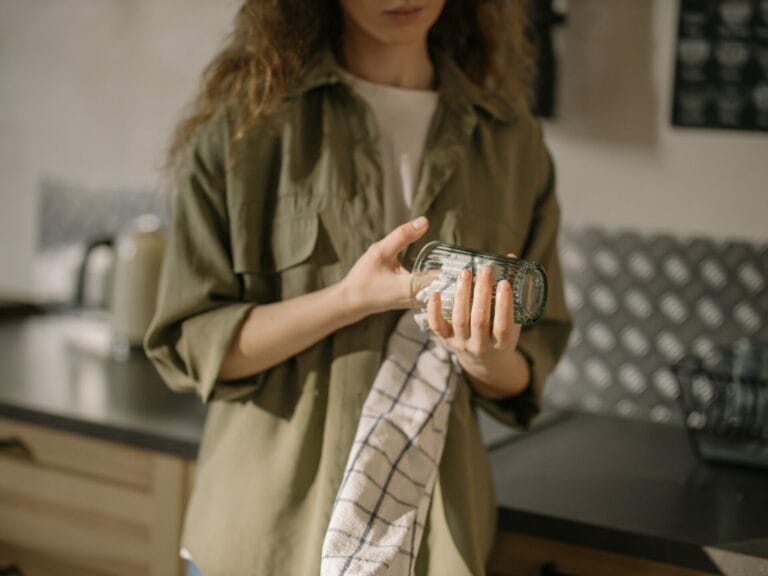 Mulher em pé com um pano de prato limpando um copo.