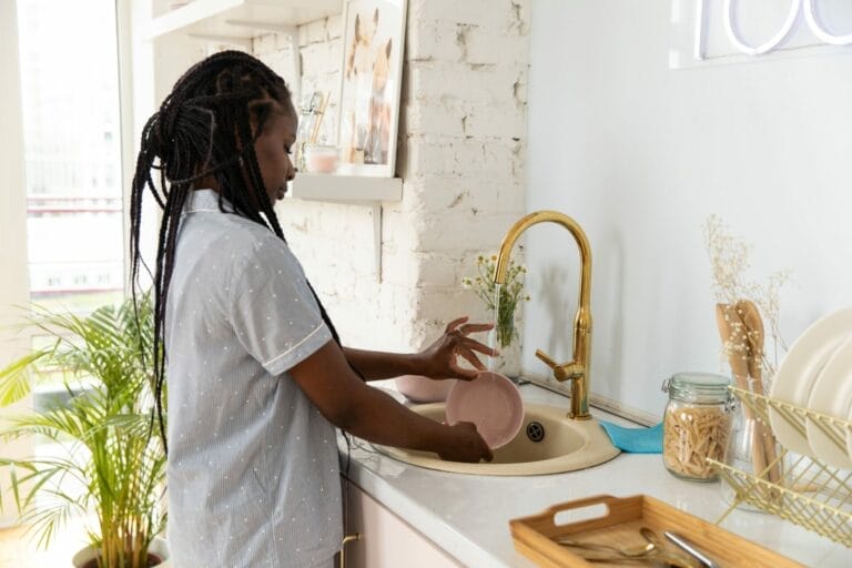 Mulher lavando louça na pia da cozinha.